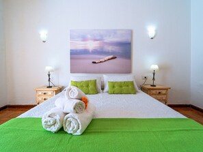 A neatly made bed with green and white bedding, two green pillows, and a rolled towel on the bed. There is a painting of a sunset on the wall above the bed. - Belvilla by OYO Holiday Home in Arico El Nuevo (Arico)