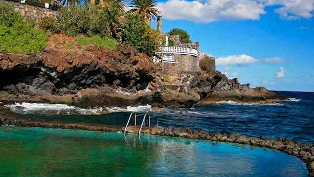 A coastal scene with a clear pool surrounded by rocky terrain and a building with a circular tower. - Belvilla by OYO Holiday Home in Arico El Nuevo (Arico)