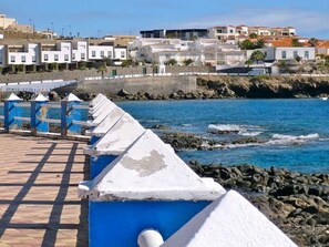 A coastal promenade with a row of white and blue structures, possibly lifeguard stations, overlooking a rocky shoreline and a residential area in the background. - Belvilla by OYO Holiday Home in Arico El Nuevo (Arico)