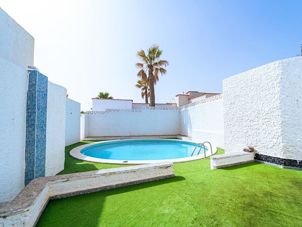 A swimming pool with a palm tree, surrounded by white walls and a tiled section.