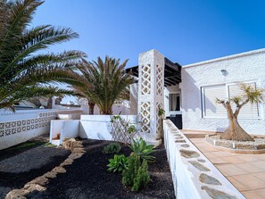 A courtyard with palm trees, a white wall with a lattice design, and a tiled floor.
