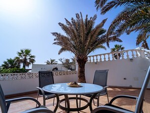 A round glass table with chairs, a palm tree, and a white wall with a decorative pattern.