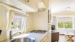 A modern kitchen with a gas stove, stainless steel sink, and a window overlooking a garden. - Beautiful Chalet Near the sea and Beach (Noordwijk)