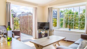 A modern living room with a sofa, a wooden coffee table, a TV, and a bottle of wine. - Beautiful Chalet Near the sea and Beach (Noordwijk)