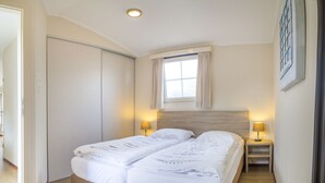 A double bed with two bedside tables, a window with curtains, and a light fixture on the ceiling. - Beautiful Chalet Near the sea and Beach (Noordwijk)