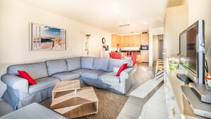 A modern living room with a sectional sofa, a coffee table, and a flat-screen TV. - Apartment in Belgium Near the Sea (Koksijde)