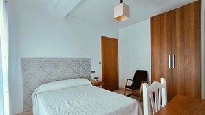 Un dormitorio con una cama, un armario de madera, una silla y una mesita.