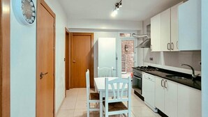 Una cocina compacta con armarios blancos, una mesa de comedor con sillas y un reloj en la pared.