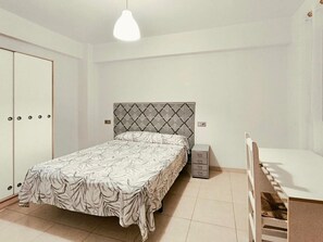 A bedroom with a bed, a wardrobe, a bedside table, and a hanging light fixture.