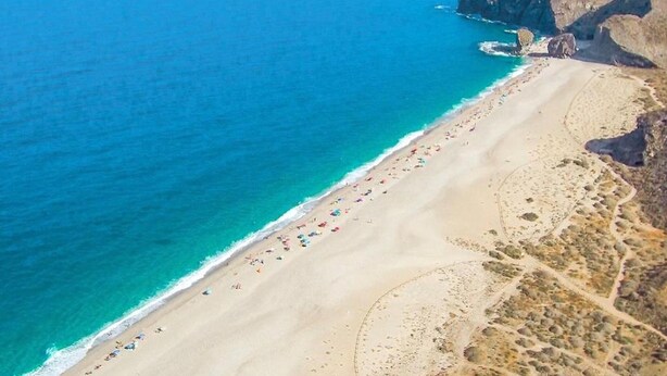 Vista aérea de una playa con aguas azul turquesa, una orilla arenosa y afloramientos rocosos.