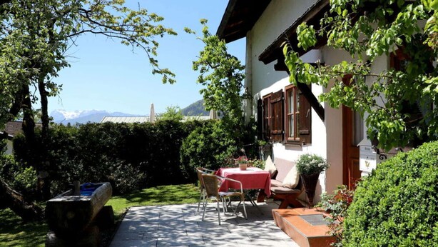 Un patio exterior acogedor con una mesa y sillas, rodeado de exuberante follaje y vistas a montañas.