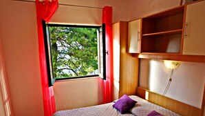 A small, cozy bedroom with a single bed, a window with red curtains, and a wooden wardrobe. - Apartments Sunset - Two Bedroom Apartment With Terrace and Sea View (Blato)