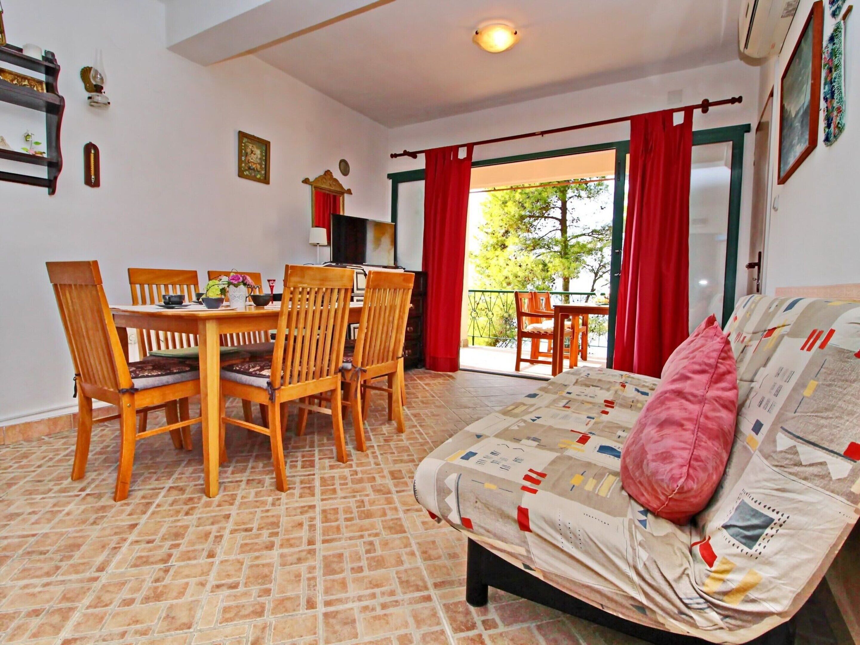 Ein Zimmer mit Esstisch und Stühlen, einem Bett mit Steppdecke und einem Balkon mit roten Vorhängen.