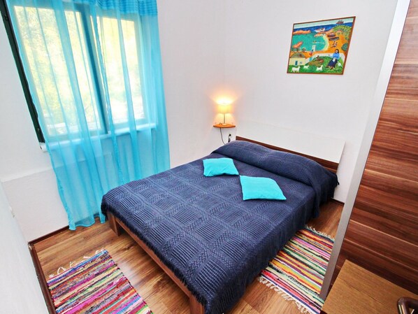 A bedroom with a bed, a wall-mounted lamp, a colorful rug, and a painting on the wall.