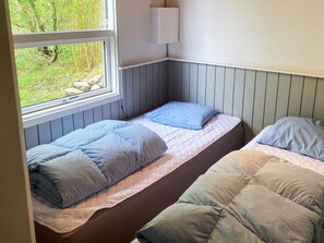 A small bedroom with two single beds, a window, and a wall-mounted light fixture.