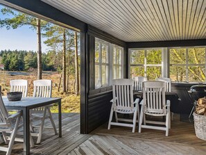 A covered outdoor seating area with a table and chairs, large windows, and a view of a forested landscape. - 6 Person Holiday Home in Bording (Bording)