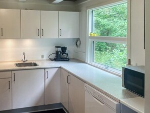A kitchen with white cabinets, a coffee maker, a sink, and a window with a view of greenery.