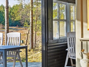 A wooden deck with white chairs and a table, overlooking a forested area.