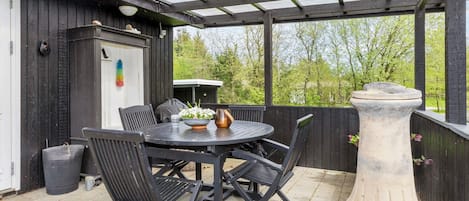 Une terrasse extérieure avec une table ronde et des chaises, un bac à fleurs en pierre et une terrasse en bois.