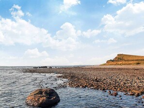 A rocky beach with a large rock in the water and a hill in the background. - 6 Person Holiday Home in Farso (Farso)