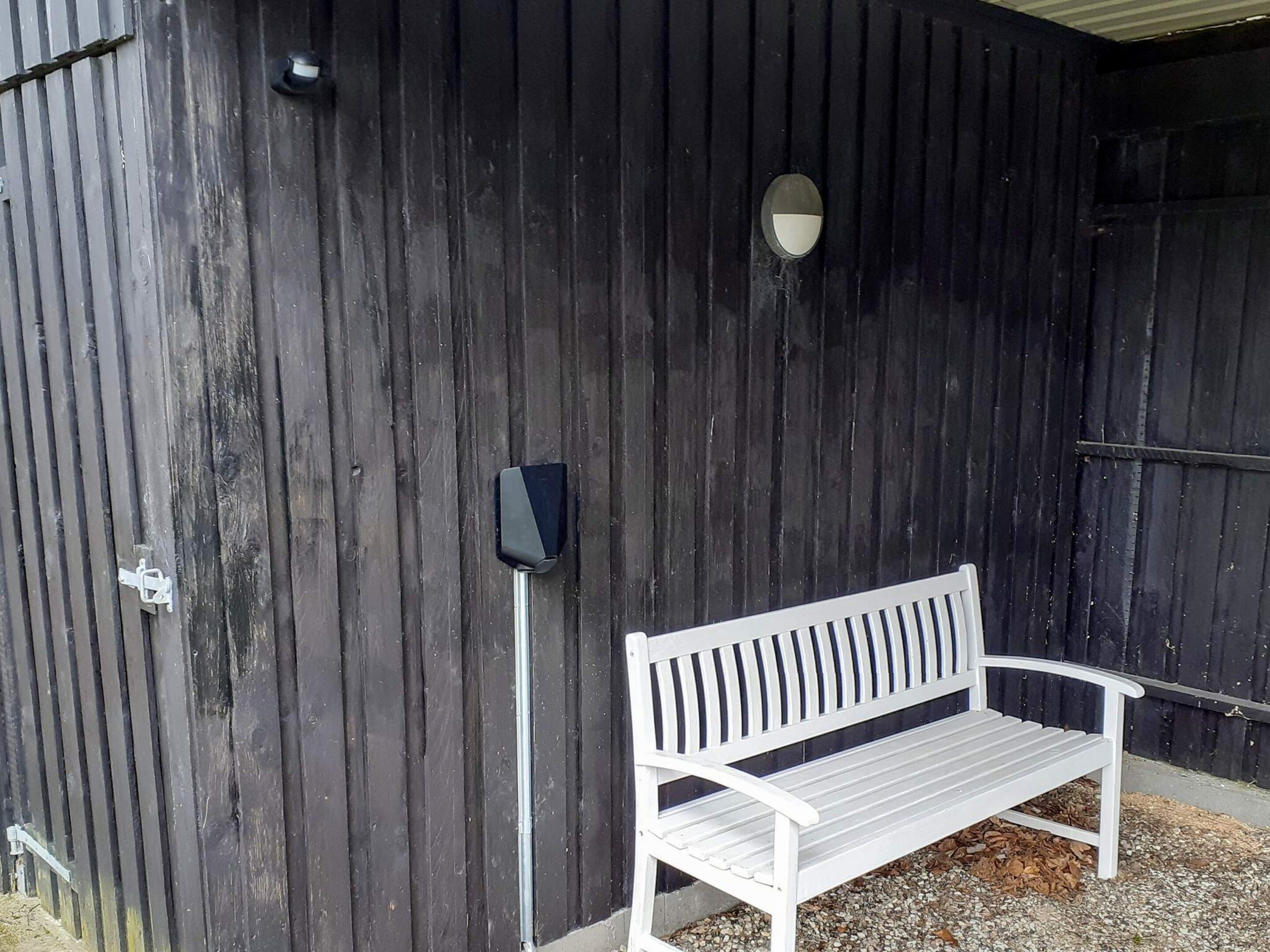 A white bench outside a dark wooden building with a metal pole and a small circular window.