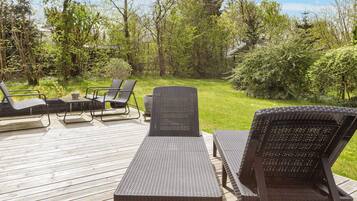 An outdoor deck with a table and chairs, surrounded by greenery.