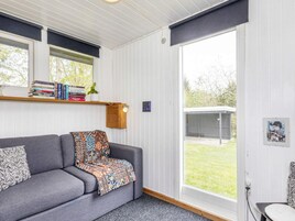 Una sala de estar acogedora con un sofá gris, una manta estampada, una estantería llena de libros y un ventanal con vistas al exterior.