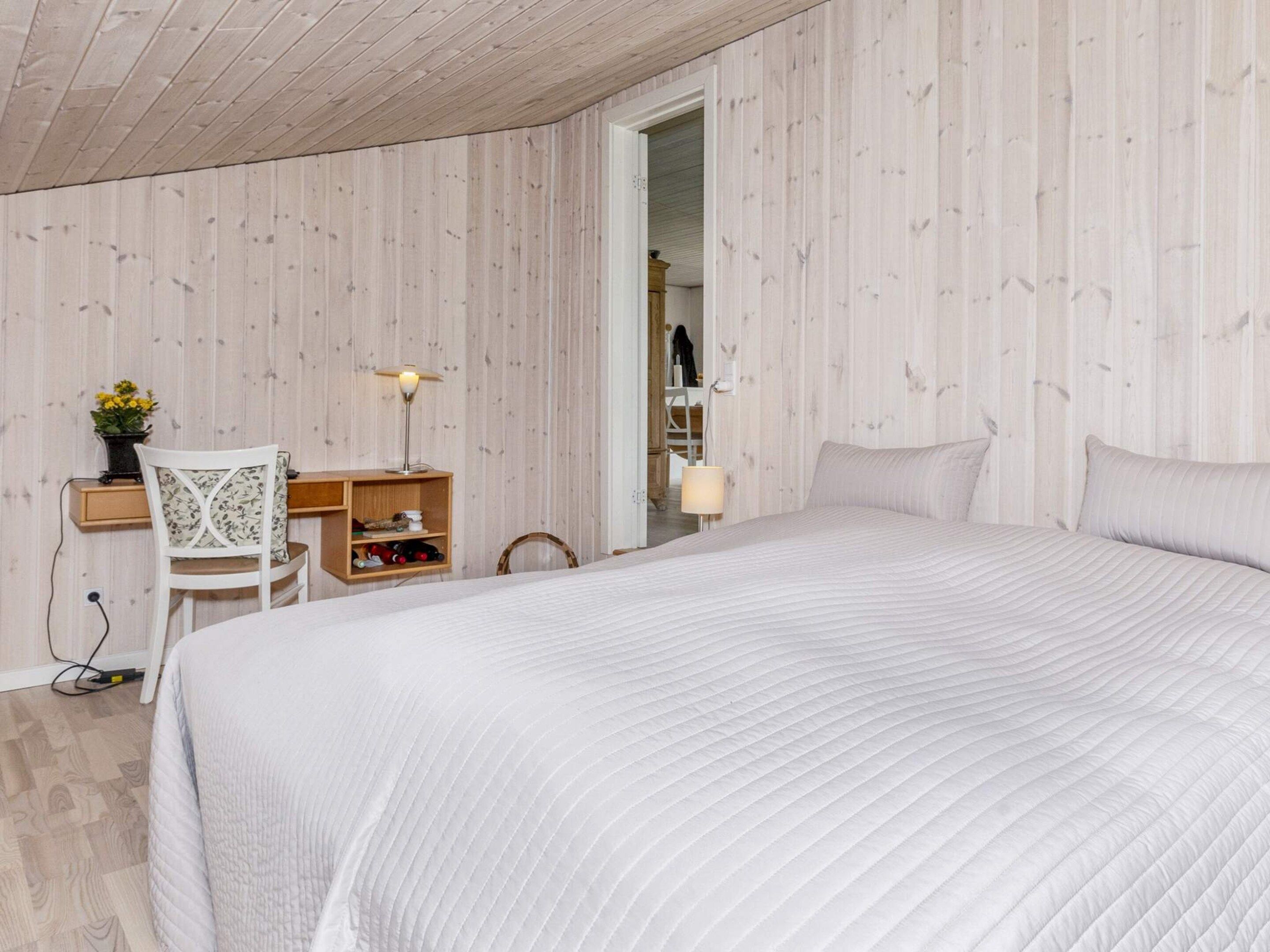 A bedroom with a large bed, a desk with a chair, a lamp, and a wardrobe.