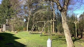 A wooden swing set with a hanging punching bag in a grassy outdoor area.