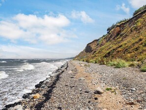 Ein felsiger Strand mit Wellen, einem klaren Himmel und einer steilen Klippe.