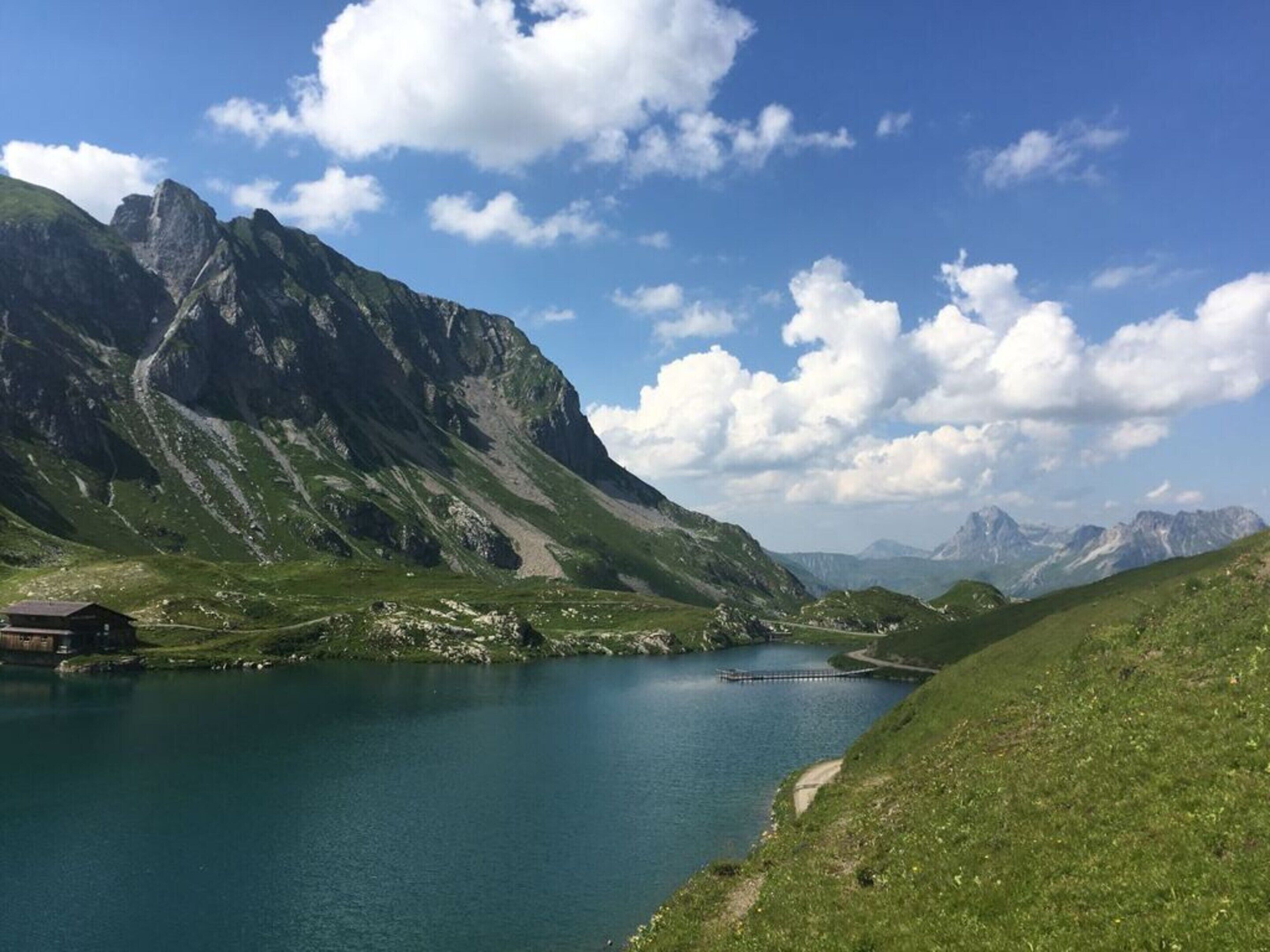 Un paisaje montañoso con un lago, un edificio pequeño y un muelle que se adentra en el agua.