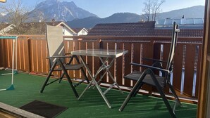 Un balcón con mesa y sillas, una valla de madera y vistas a las montañas.