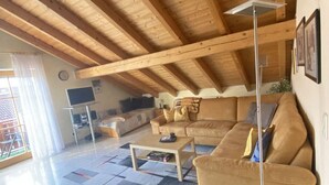 Un salón amplio con techo de madera alto, un sofá grande color beige, una mesa de centro y un televisor de pantalla plana.