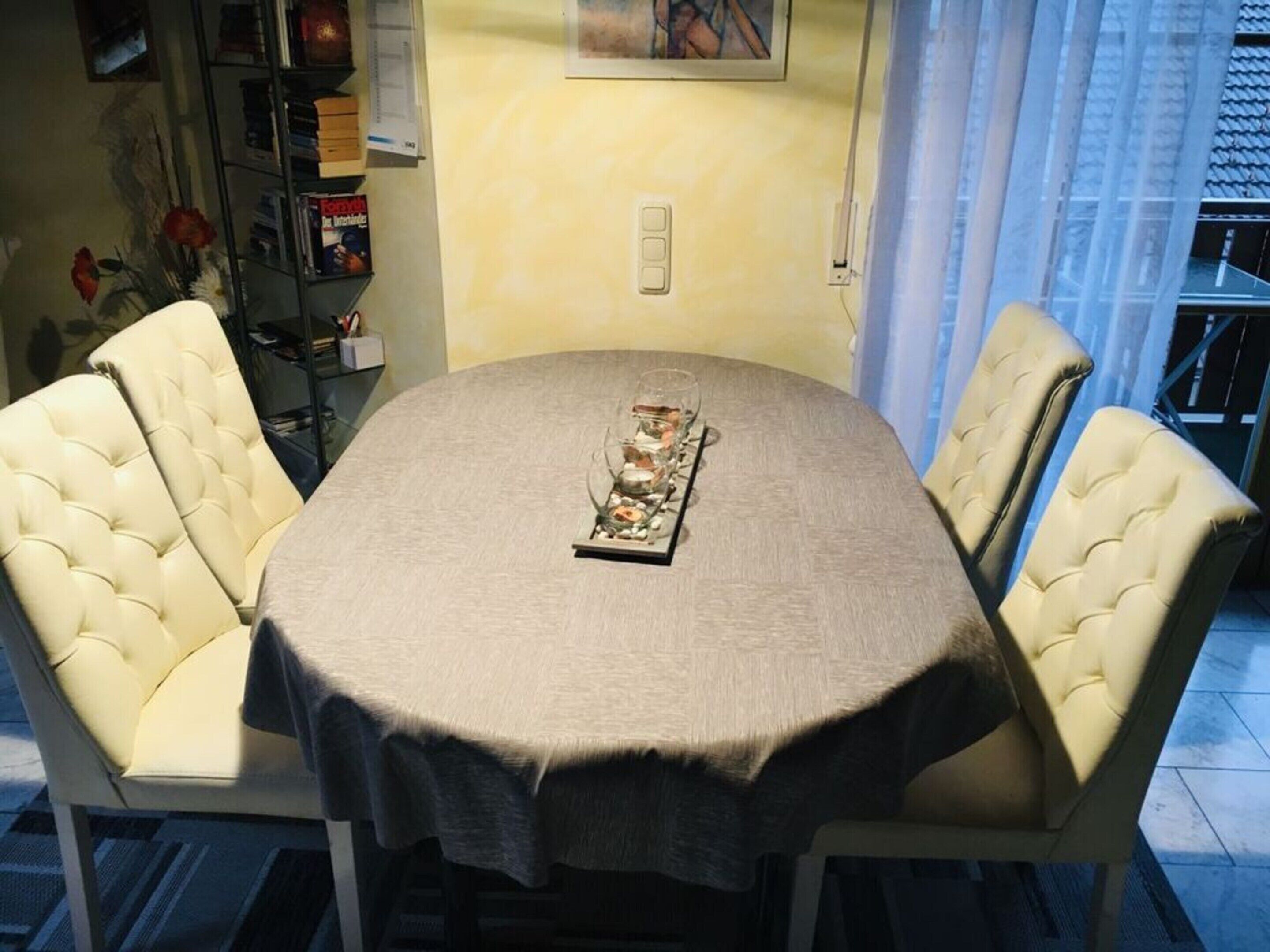 Una mesa de comedor redonda con mantel beige, rodeada por cuatro sillas tapizadas en beige.