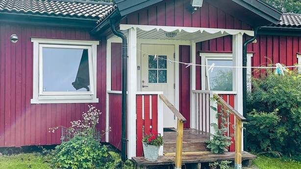 Een rode houten woning met een veranda, een raam en een deur.