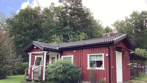 Een rode houten woning met een veranda, een kleine tuin en een heldere lucht.