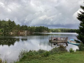 A calm lake with a dock and a small boat, surrounded by dense forest and overcast sky.