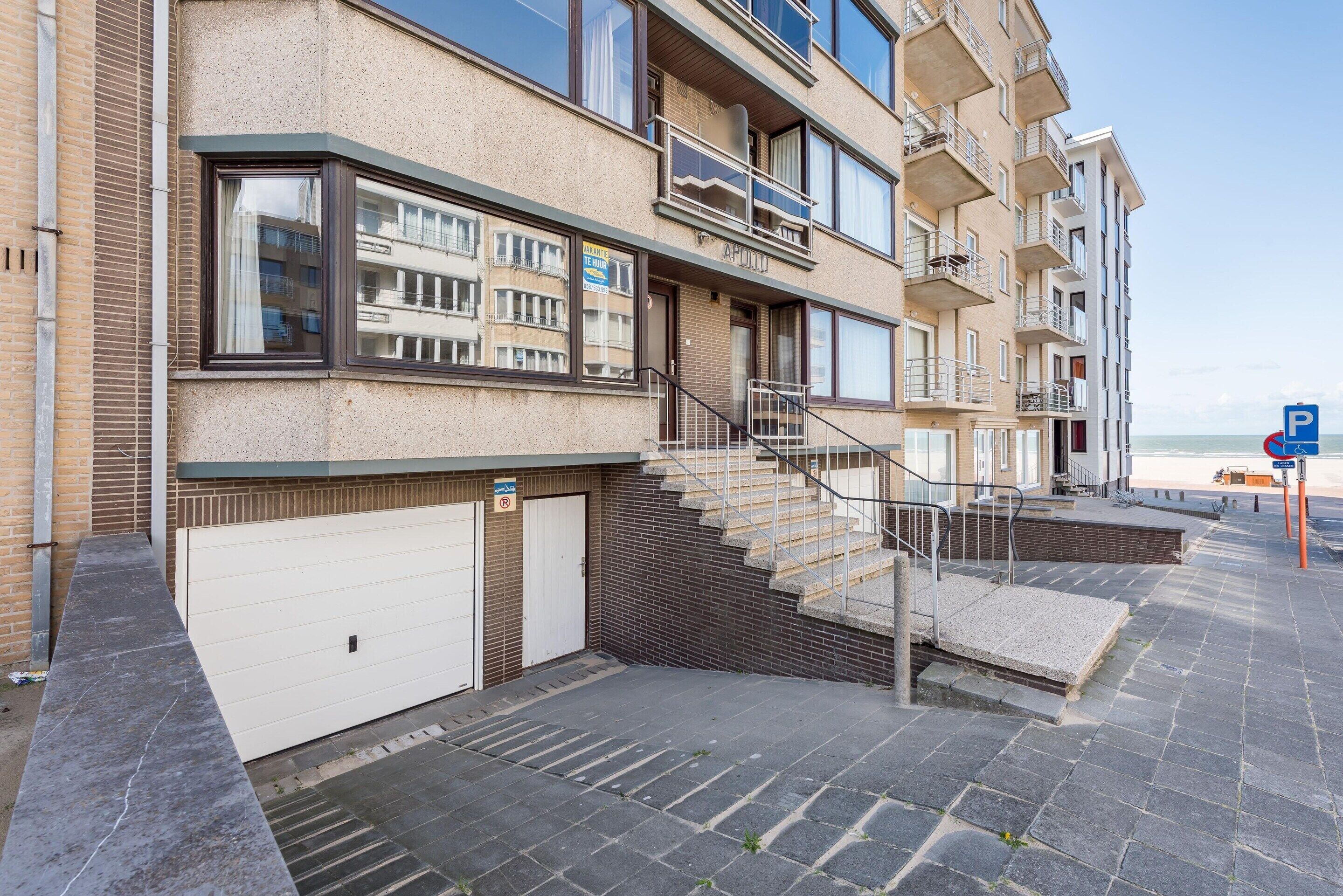 A multi-story residential building with a garage, a staircase leading to the upper floors, and a view of the sea.