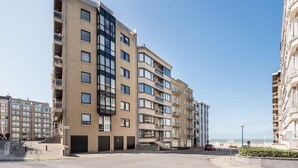 Een meerlaags appartementencomplex met balkons, een parkeerplaats en een helder uitzicht op zee.