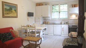Ett kompakt vardagsrum med en matplats, en röd soffa, ett litet bord och ett kök med vita skåp och en spis.