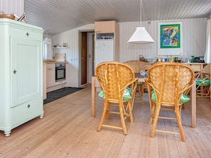 A dining area with wicker chairs and a white table, a kitchen with a white refrigerator, and a wooden cabinet.