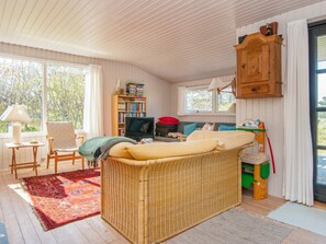 A cozy room with a wicker sofa, a television, a bookshelf, and a window with curtains. - 6 Person Holiday Home in Glesborg (Glesborg)