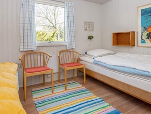 A room with a bed, two chairs, a colorful striped rug, a window with curtains, and a framed picture on the wall.