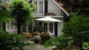 A two-story house with a balcony, a patio with outdoor furniture, and a garden area. - Charming Home w/ Garden (Ostend)