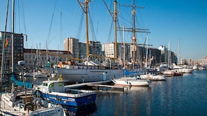 A marina with multiple boats docked, a cityscape in the background, and a clear blue sky. - Charming Home w/ Garden (Ostend)