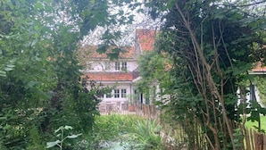 A garden with a wooden fence, dense foliage, and a house in the background. - Charming Home w/ Garden (Ostend)