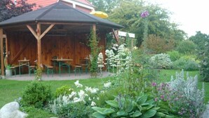 A wooden pavilion with outdoor seating, surrounded by a garden with various plants and rocks. - Siems Modern Retreat (Grube)