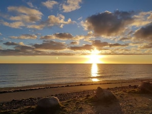 A sunset over a calm sea with a rocky shoreline and a paved path. - Siems Modern Retreat (Grube)