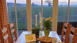 A wooden table set for two with a view of a field and mountains through large windows. - Siems Modern Retreat (Grube)