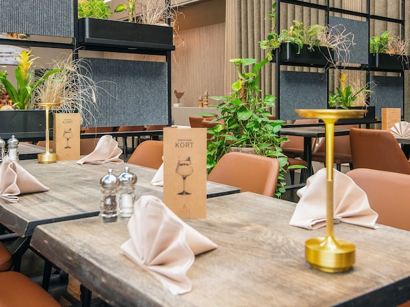 A restaurant setting with wooden tables, chairs, and potted plants.